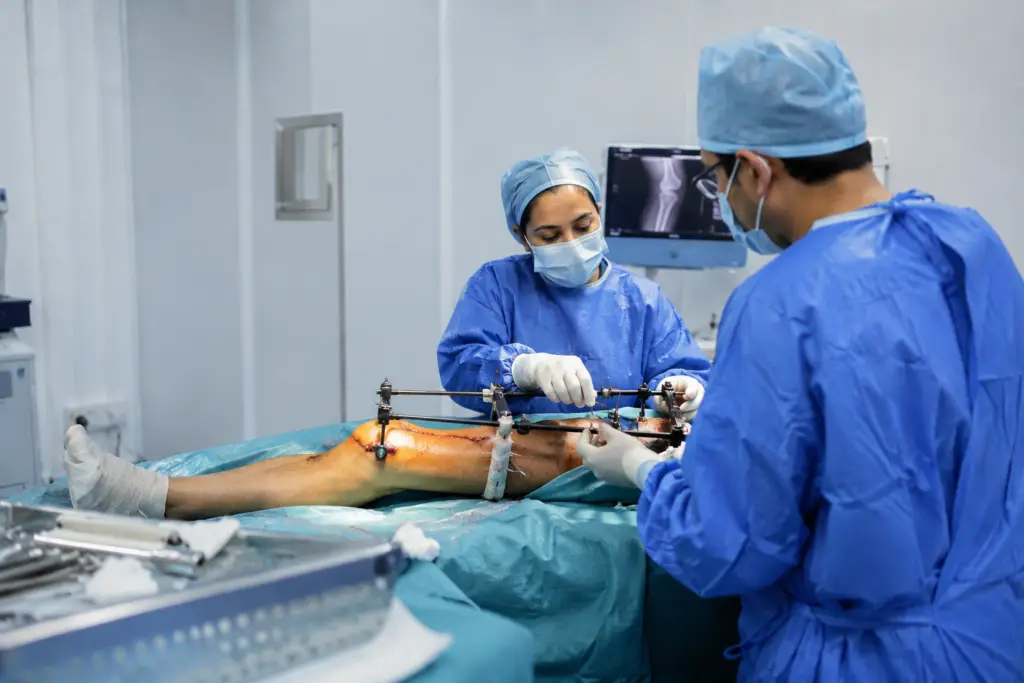 Surgeons in blue scrubs and masks perform leg surgery using an external fixator on a patient’s leg.