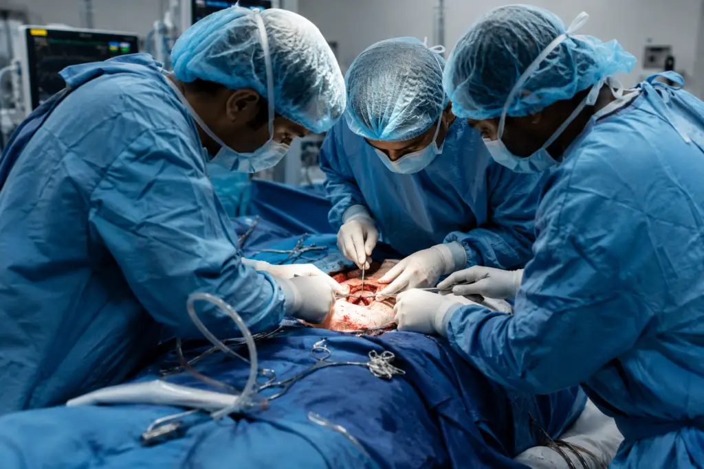 Surgeons in blue scrubs and masks perform an open surgical procedure around a patient in the operating room.