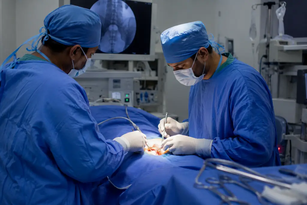 Two surgeons in blue scrubs and masks perform an operation, using surgical instruments over a patient on the operating table.
